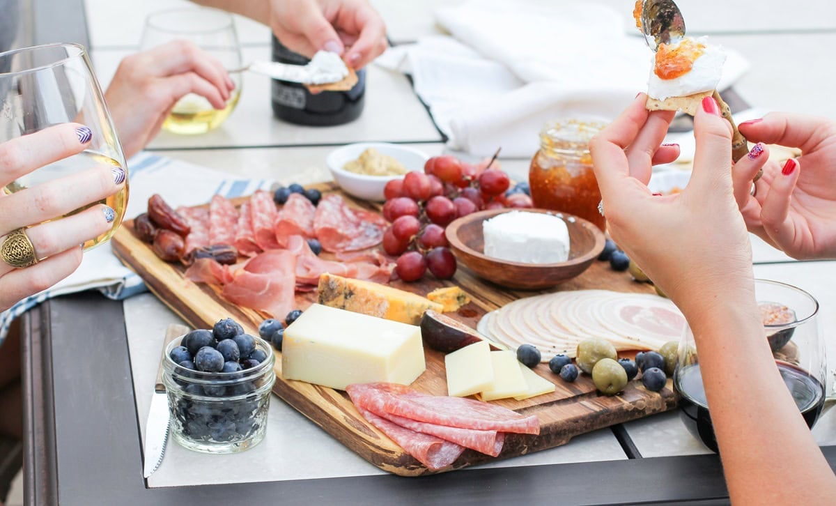 Three women enjoying a charcuterie board, making meat, cheese, and spread pairings.