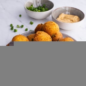 Plate full of hush puppies sprinkled with green onions with dipping sauce in the background.