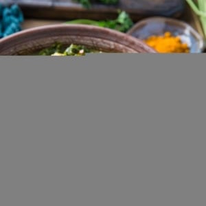 close up turmeric chicken soup in a brown bowl with a blue napkin to the side.