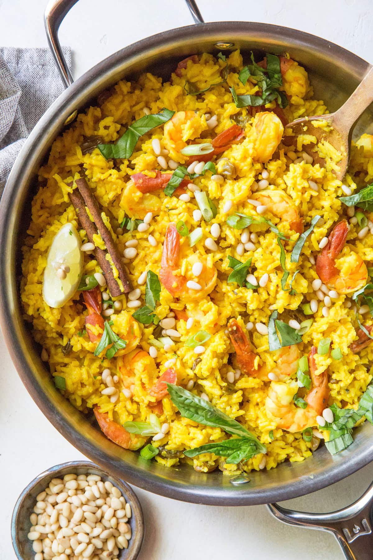 Stainless steel skillet full of shrimp biryani with pine nuts and fresh herbs sprinkled on top.