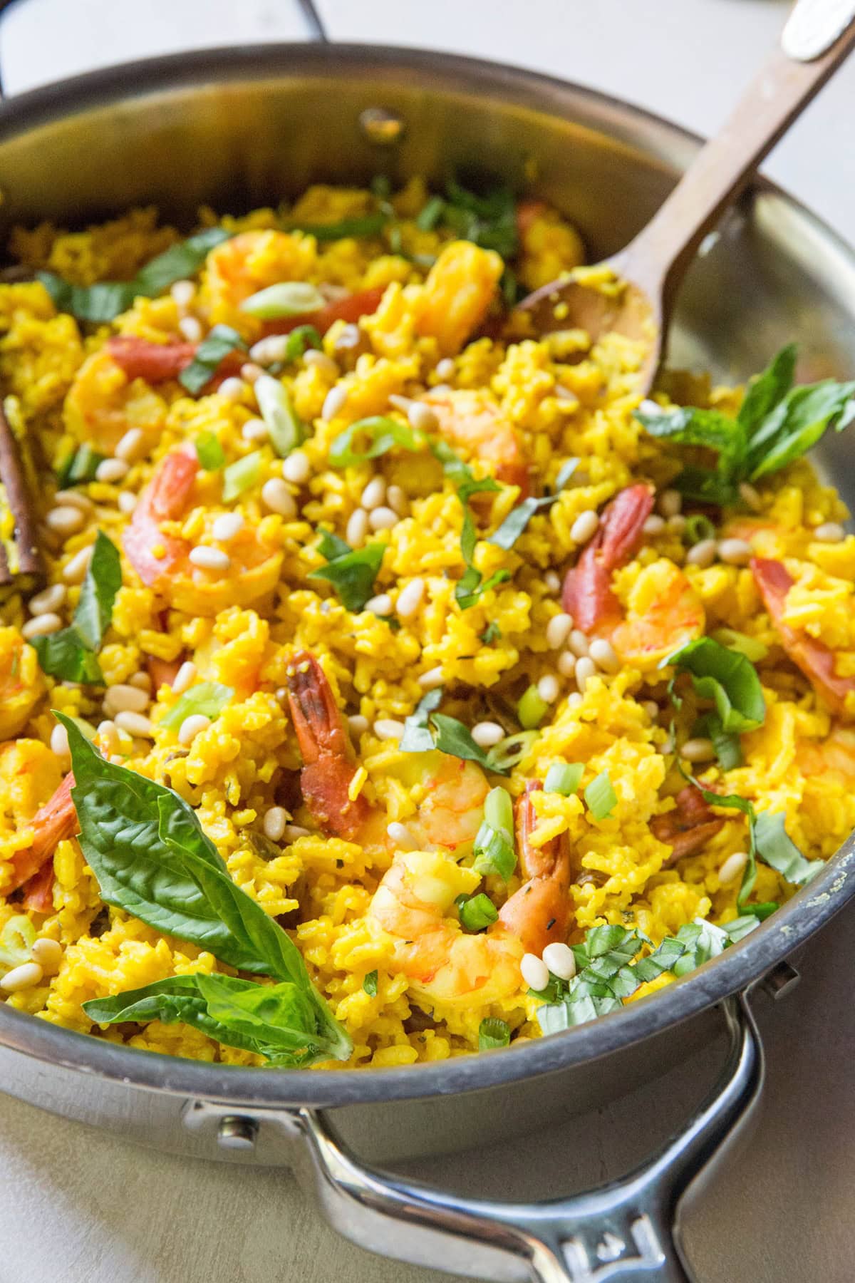 Stainless steel skillet full of shrimp biryani with fresh veggies and pine nuts on top.