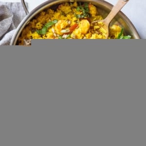 Indian Shrimp Biryani in a stainless steel skillet with a bowl of pine nuts to the side.