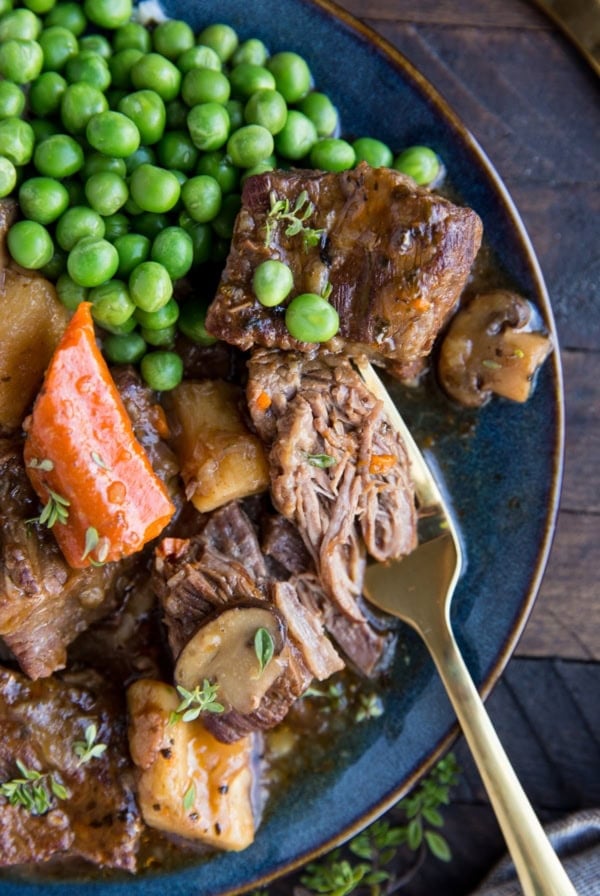 Large blue plate full of beef and stewed vegetables and a fork shredding a piece of beef.