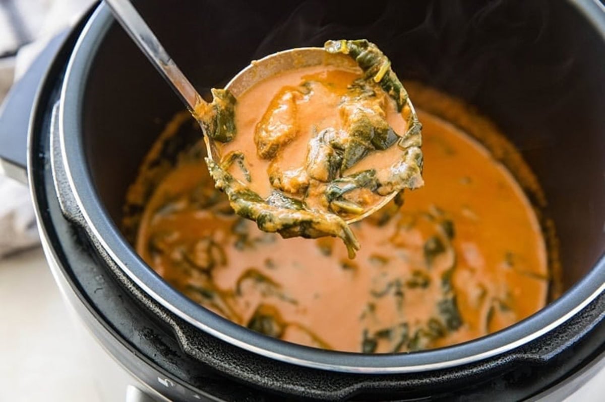 Instant pot full of Indian lamb curry with a ladle scooping a portion out.