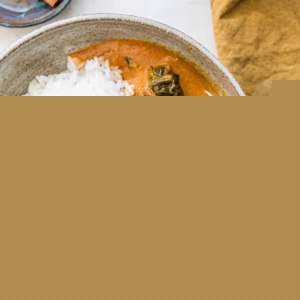 Large bowl of lamb curry with white rice with a golden napkin to the side and a bowl of cinnamon sticks.