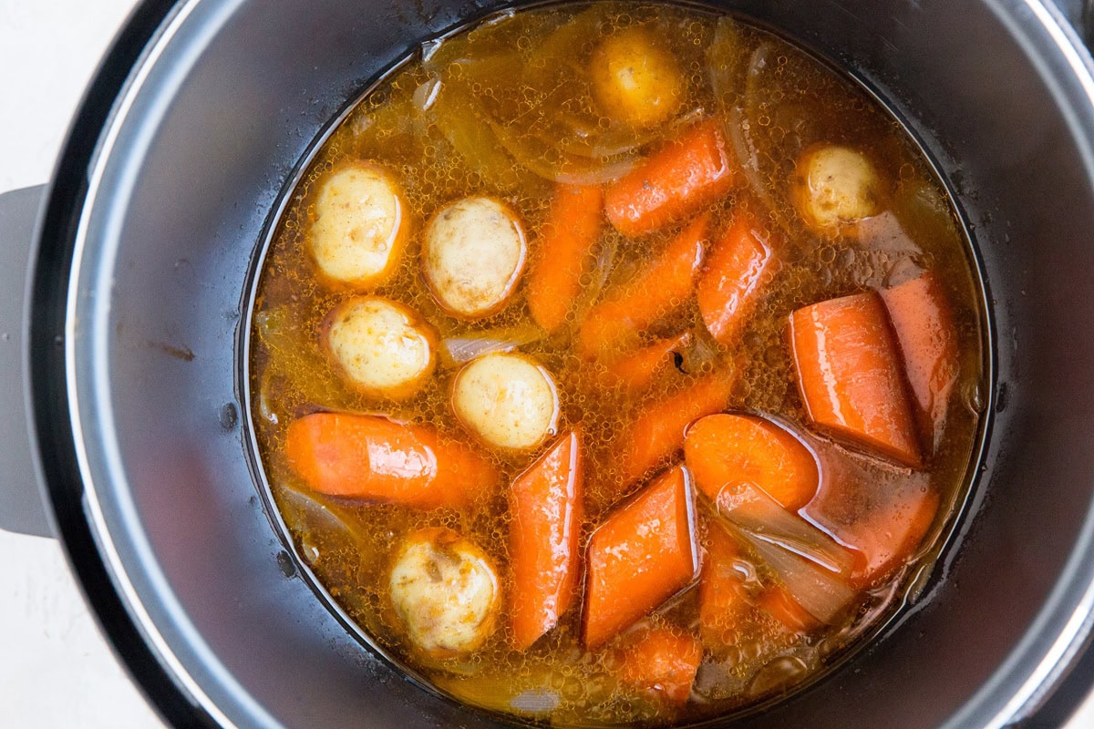 Electric pressure cooker pot filled with cooked carrots, potatoes, and onions in a rich brown Instant Pot Pot Roast broth.