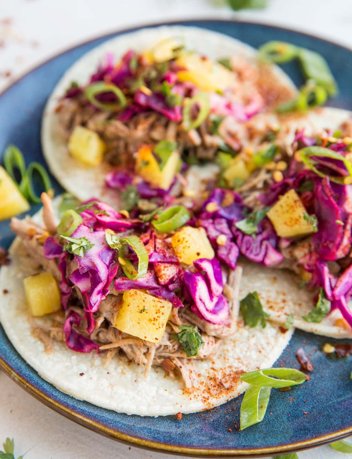 Shredded Pineapple Pork Tacos with cabbage slaw and green onion on a blue plate, ready to serve.