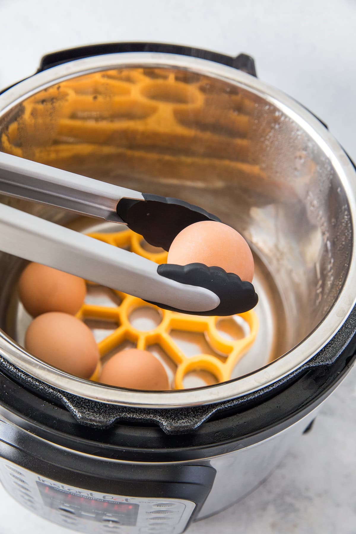 Tongs lifting an egg out of an instant pot that has been freshly cooked.