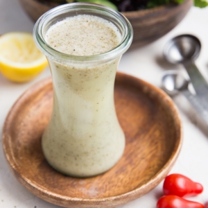 Italian salad dressing in a glass container with fresh tomatoes to the side and a salad in the background.