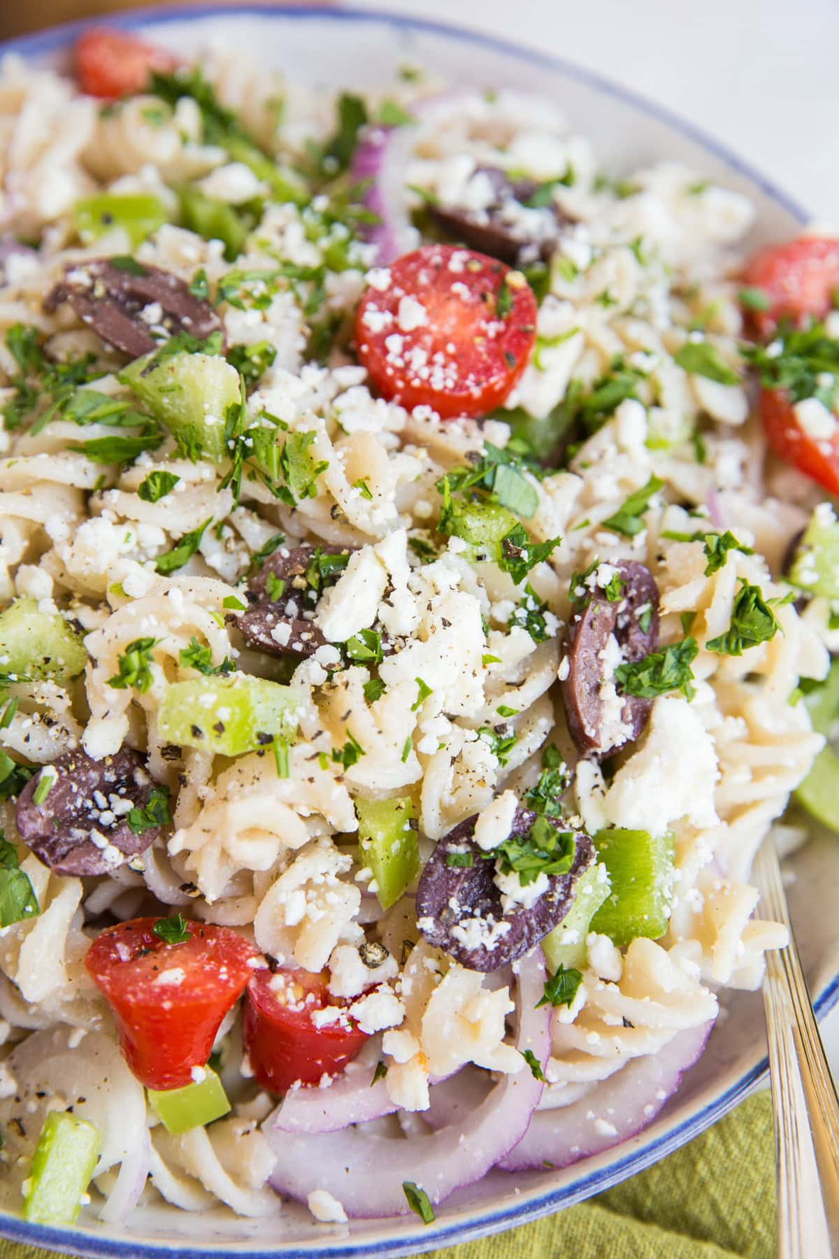 Italian pasta salad recipe in a large white bowl with a blue rim and a silver spoon to the side, ready to serve. Packed with fresh vegetables and a light dressing for a delicious side dish.
