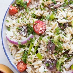 Gluten free Italian pasta salad in a large bowl with a bowl of cherry tomatoes to the side. Pasta noodles, red onions, bell peppers, cherry tomatoes, feta cheese, and more.
