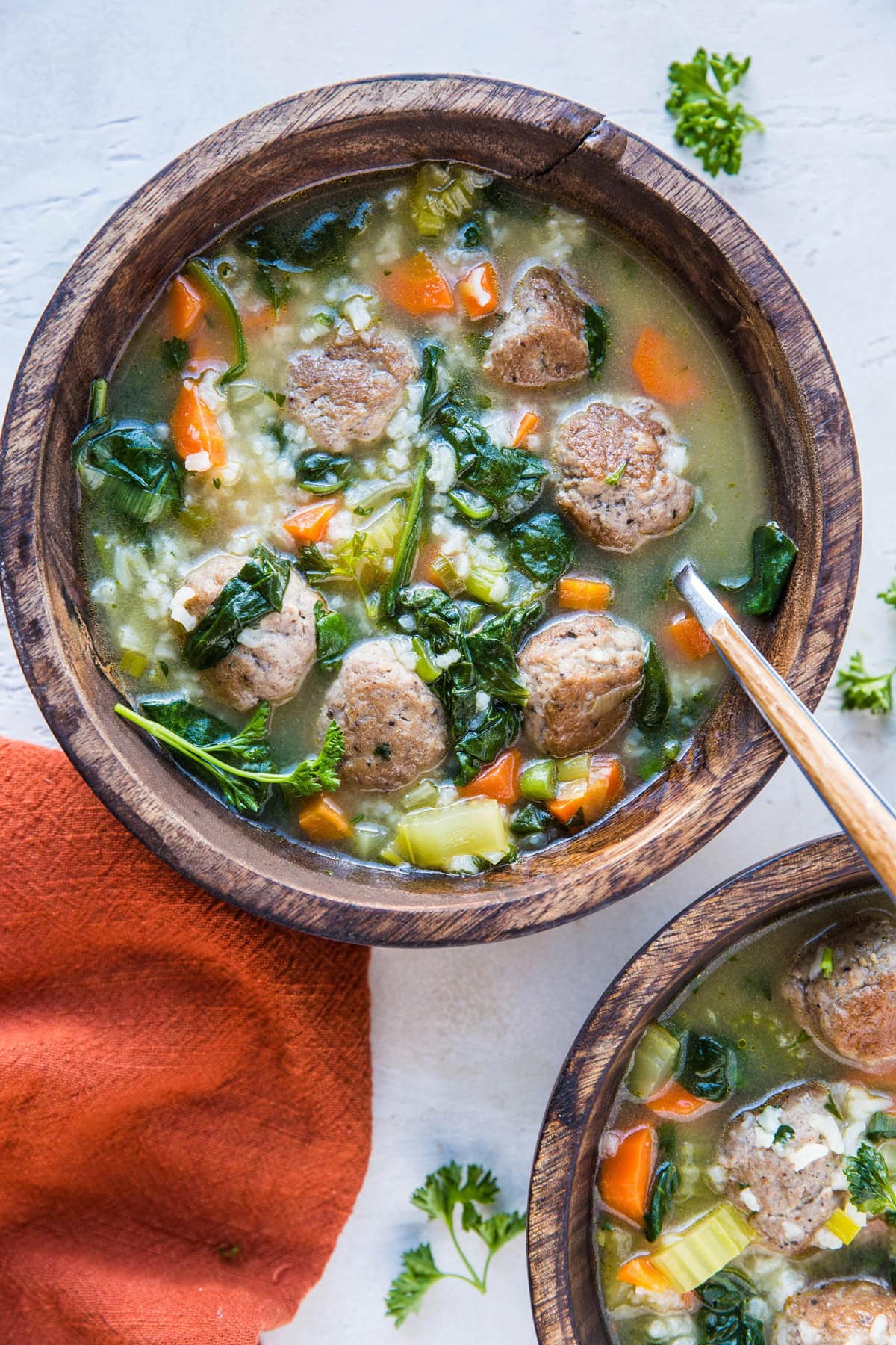 Two bowls of Italian Wedding Soup with rice. A red napkin and fresh parsley to the side.