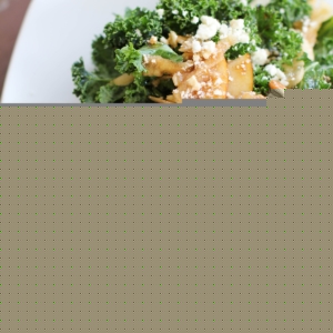 Massaged Kale Salad with Apple, Pear, Gorgonzola and Roasted Pecans on a white plate with a red napkin to the side.