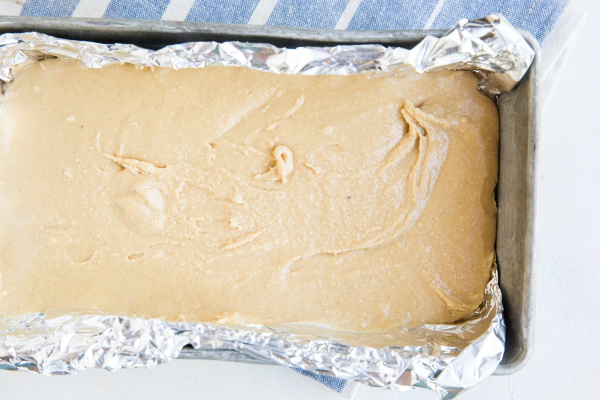 Peanut butter layer in a loaf pan lined with foil for peanut butter bars.
