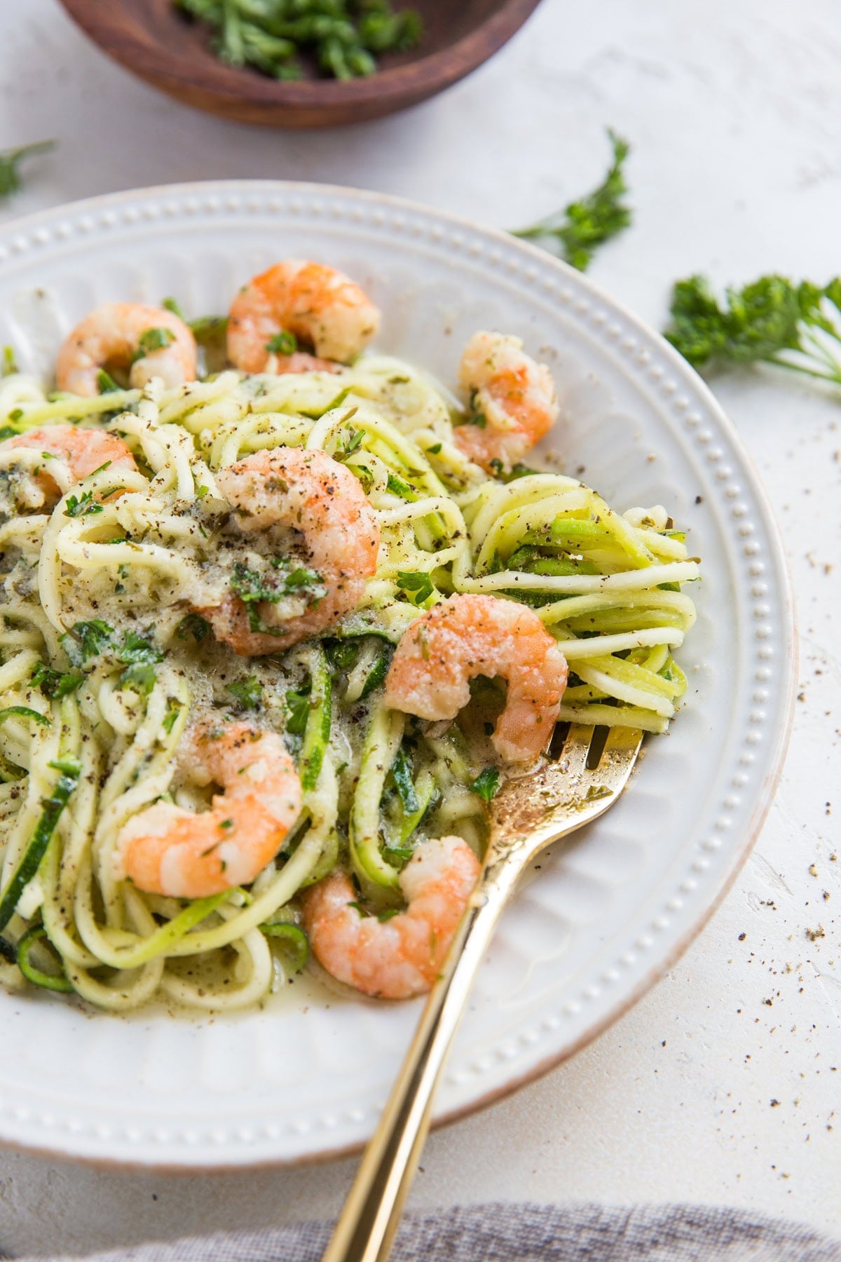 Zucchini noodles and shrimp on a white plate with a golden fork twirling some of the zoodles. Ready to serve.