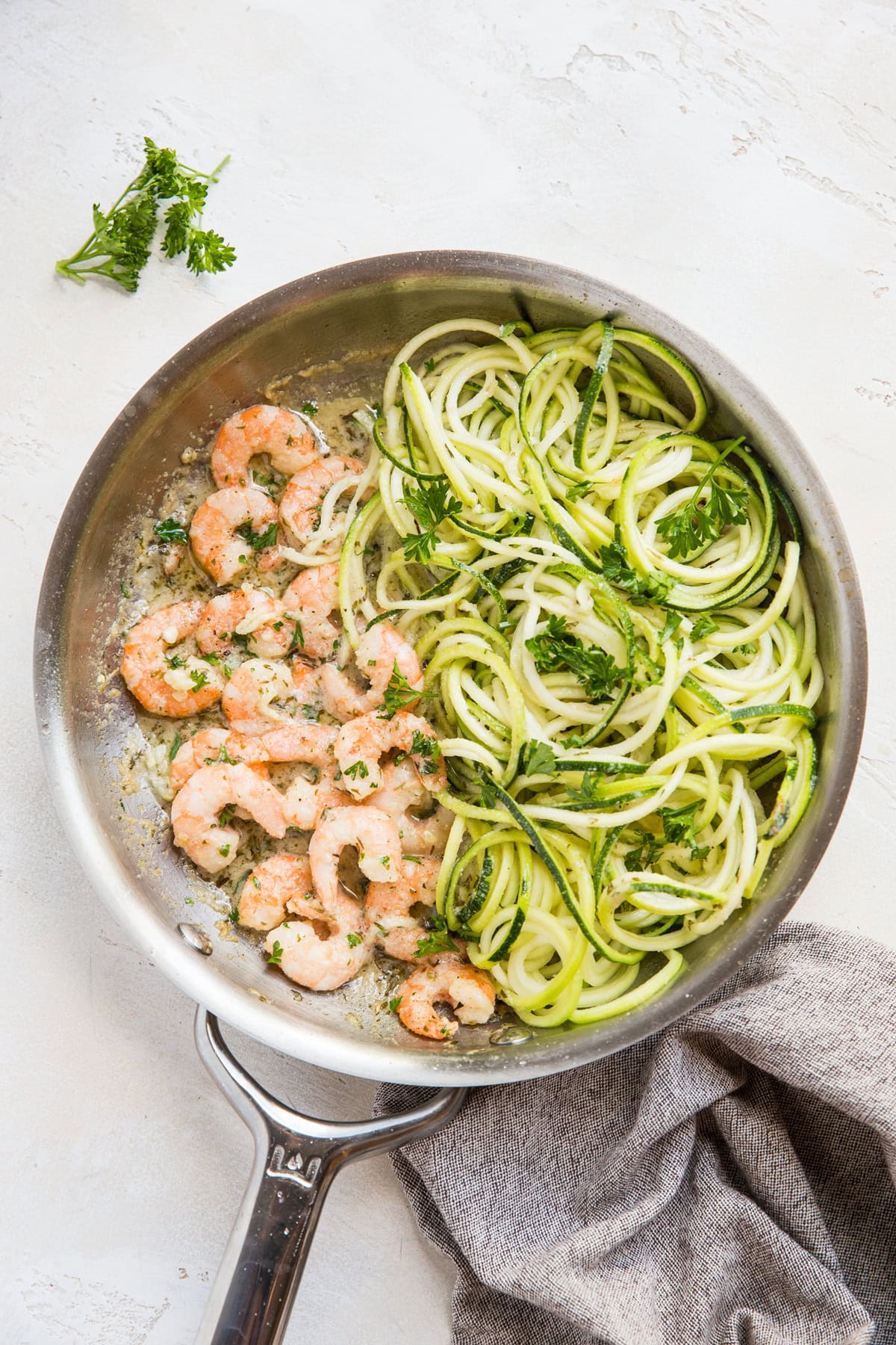 Stainless steel skillet with zucchini noodles on one side and cooked shrimp on the other side. Ready to be mixed together to make zucchini noodle shrimp scampi.
