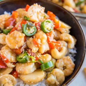 Large ceramic bowl full of kung pao shrimp on top of white rice with chop sticks to the side.