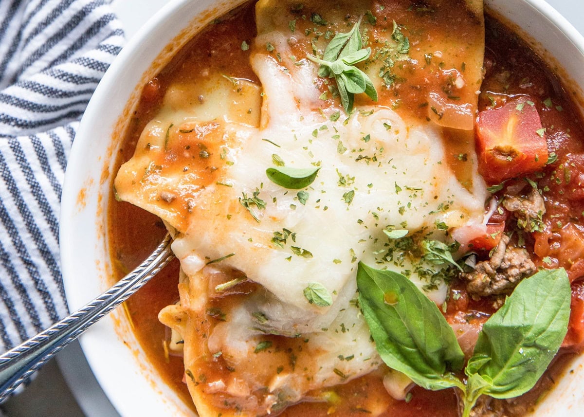 large white bowl of lasagna soup with melted cheese on top and a silver spoon digging in.