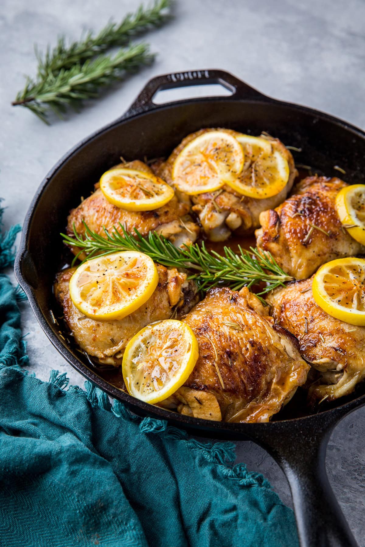 large cast iron skillet full of lemon garlic braised chicken thighs with slices of lemon and a blue napkin.