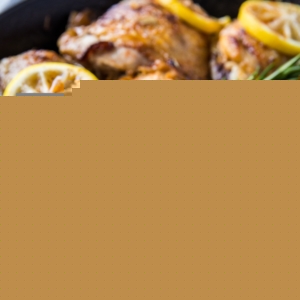 Braised skin-on chicken thighs in a cast iron skillet with fresh rosemary and lemon slices.