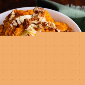 Mashed sweet potatoes in a white bowl with melted butter on top and chopped pecans. A teal tea towel to the side.