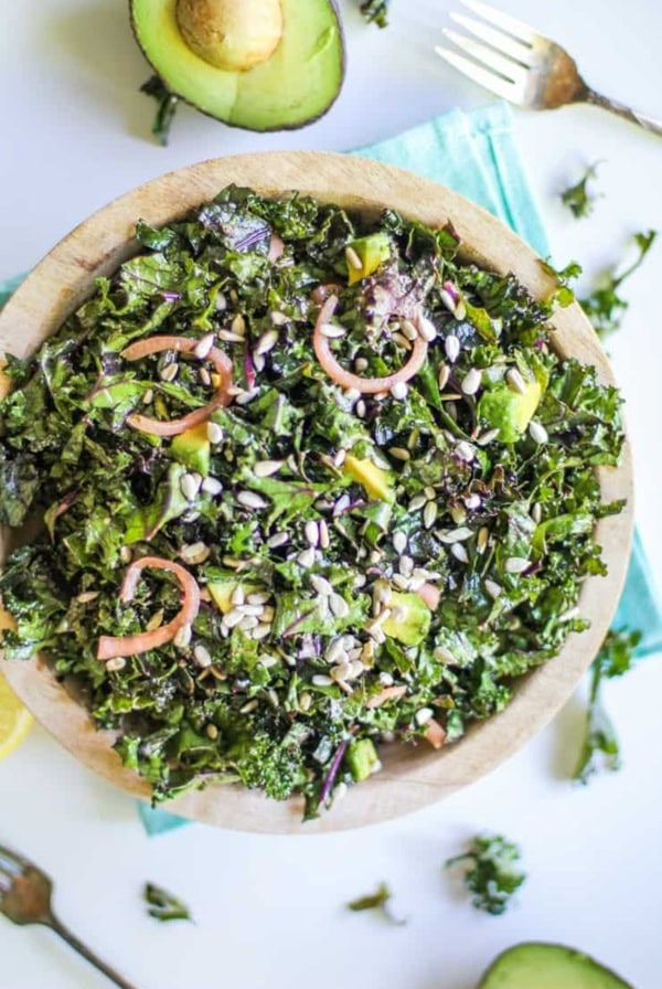 Large bowl full of massaged kale salad with pickled red onions and avocado.