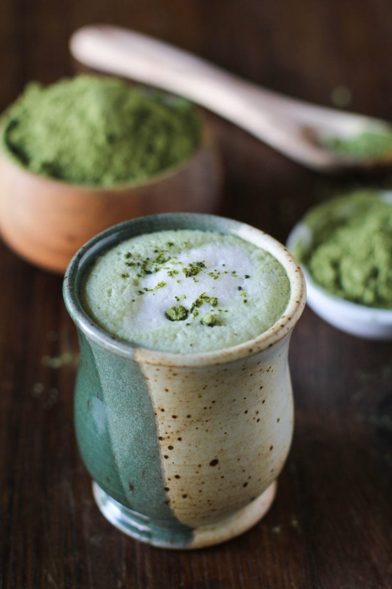 Matcha Green Tea Latte in a fancy ceramic mug with a pile of matcha in the background.