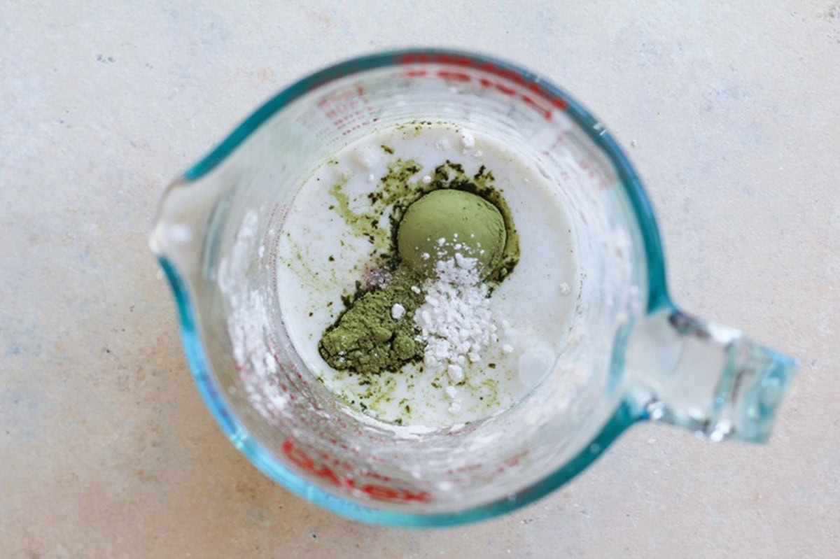 Flour, matcha powder and milk in a measuring cup to be stirred together.