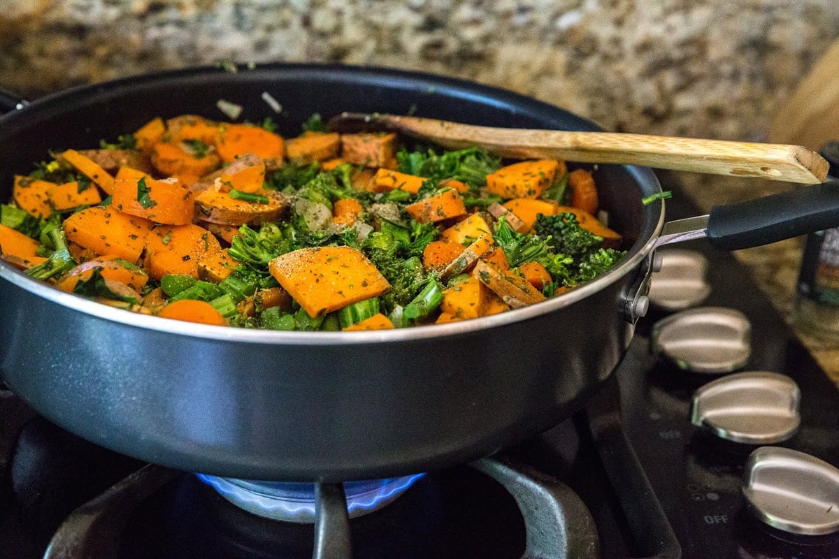 Vegetables seasoned with seasonings in a very large skillet cooking on the stove top.
