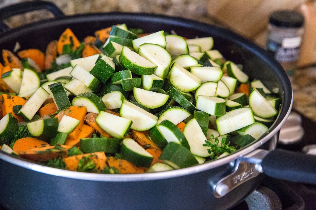 Very large skillet with a deep lip cooking vegetables on the stove top.
