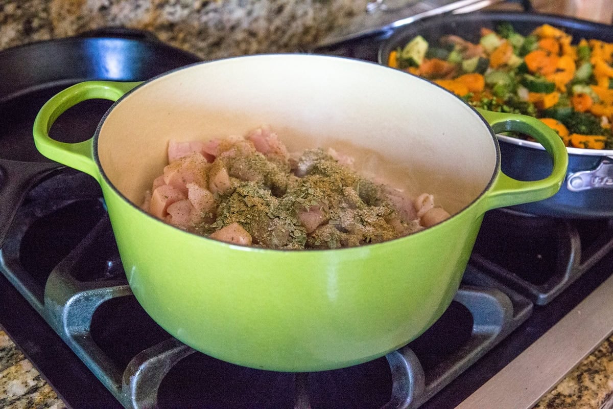 Raw chopped chicken sprinkled with Italian seasoning in a large Dutch oven on the stove top, ready to be cooked.