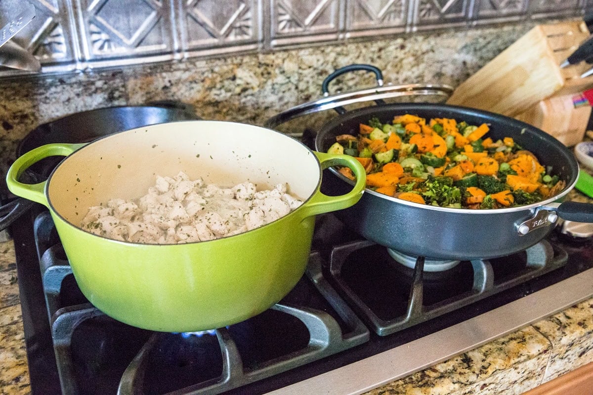 large pot of chopped chicken and large skillet full of vegetables cooking on the stove top