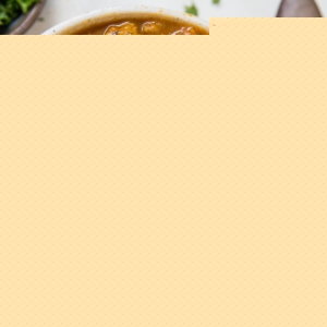 Big bowl of soup with fresh vegetables and meat. A red napkin, spoon, and fresh herbs to the side of the bowl.