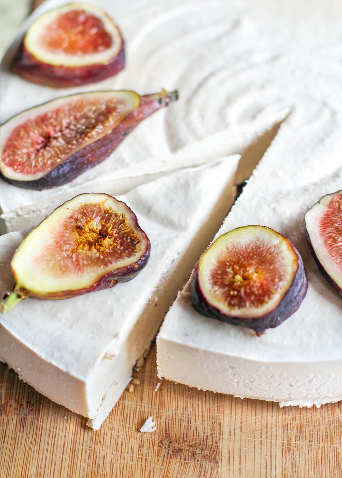 Whole cheesecake on a wooden cutting board with a slice taken out. Sliced figs sit on top of the cheesecake.