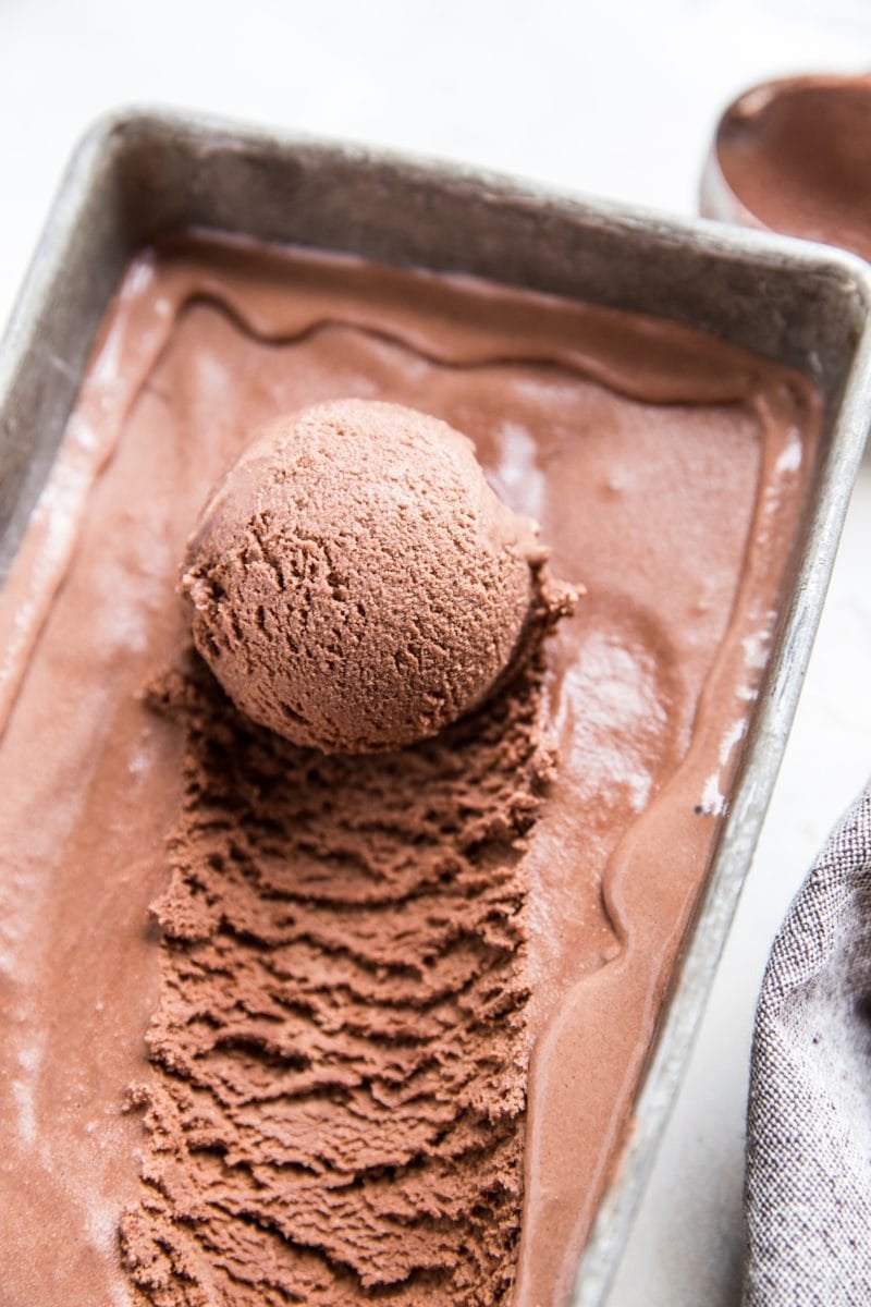 container of homemade no churn chocolate ice cream with scoop taken out and a napkin to the side.