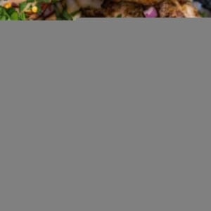 grilled orange ginger chicken thighs in a large casserole dish with chopped red onions, red pepper flakes, and parsley sprinkled on top.