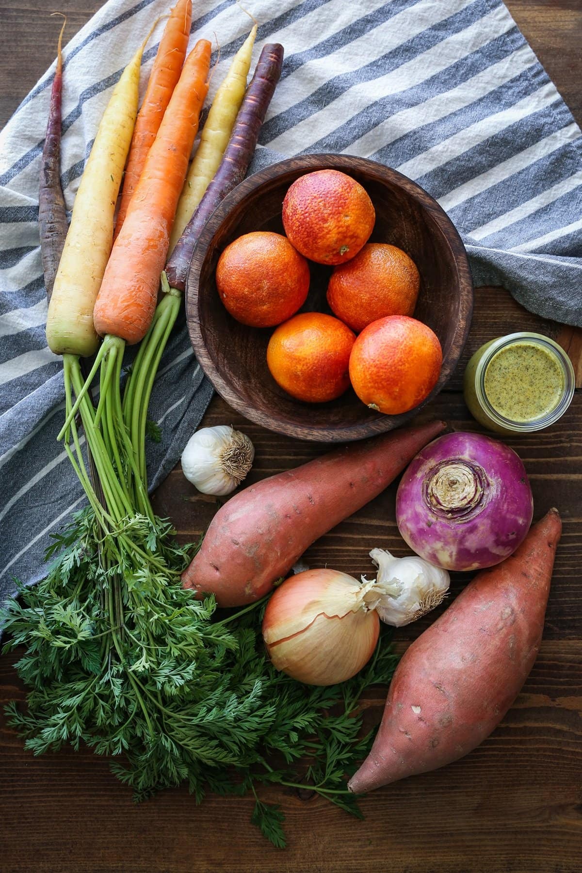Assorted root vegetables sitting on a wooden table, waiting to be chopped and roasted.
