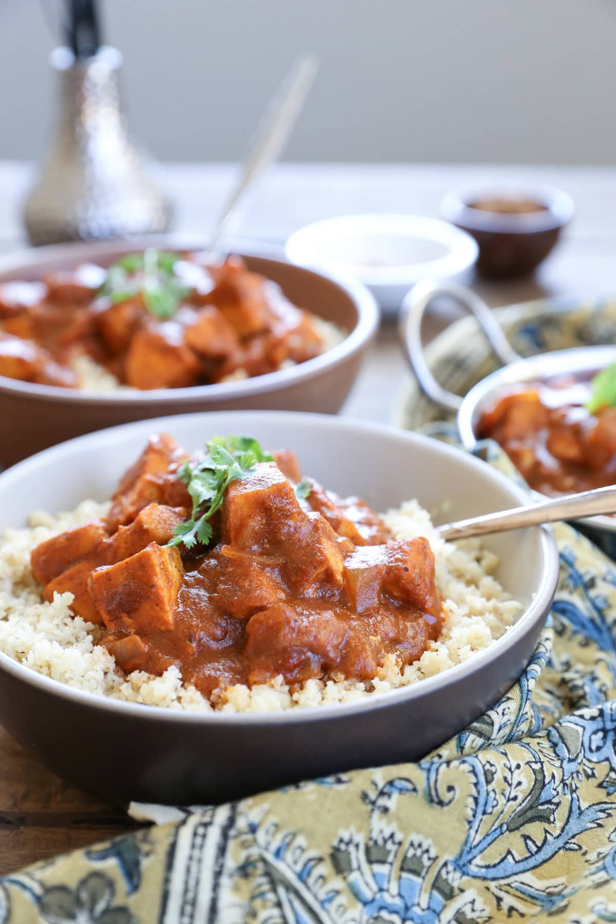 large bowl full of butter chicken on top of cauliflower rice with a decorative napkin nearby.