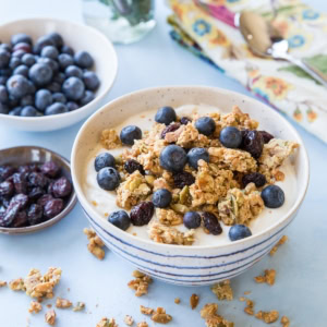 white and blue striped bowl full of yogurt with paleo granola and fresh blueberries on top. Clusters of granola all around the bowl.