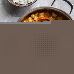 Stainless steel skillet full of chicken panang curry. A bowl of rice and chopsticks to the side.