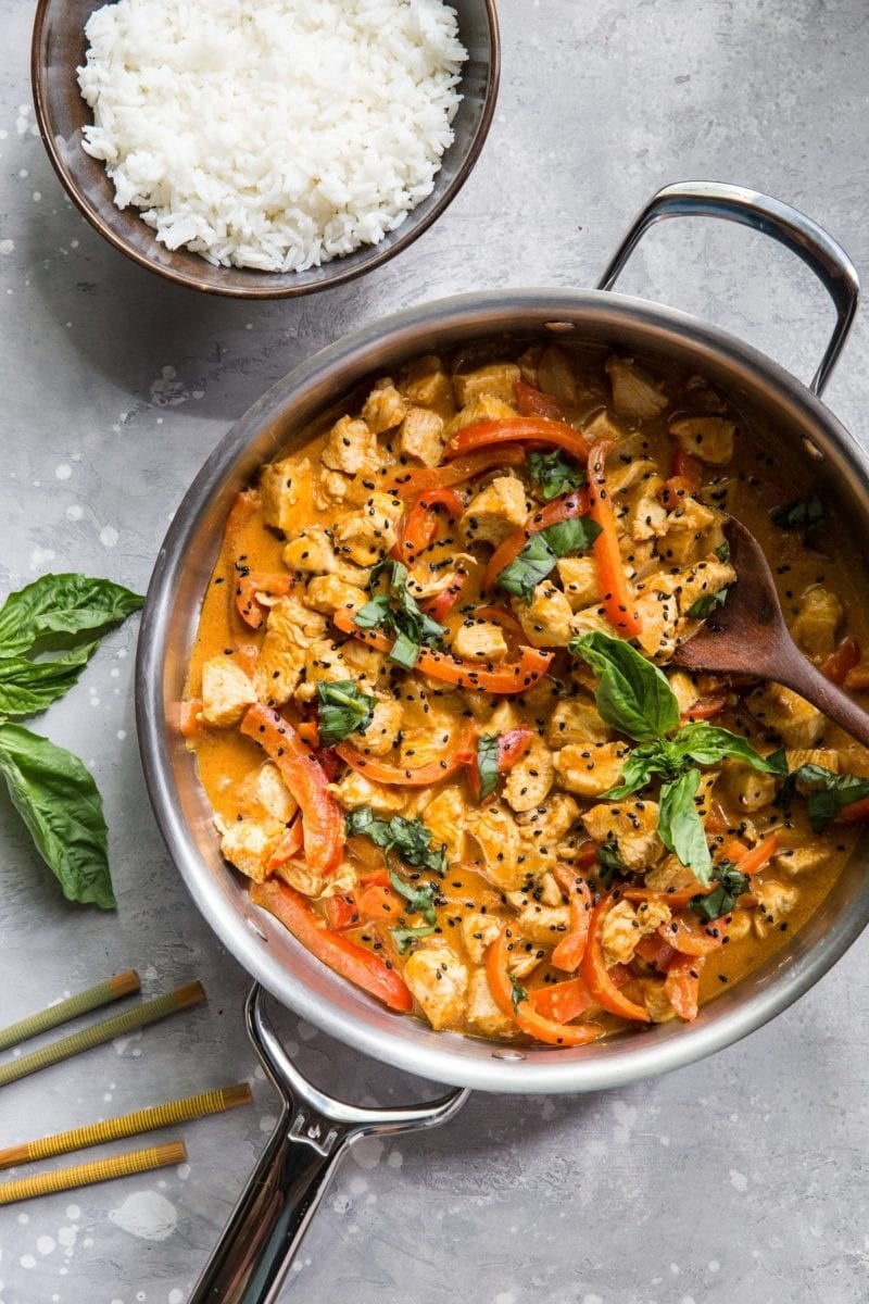 Stainless steel skillet full of chicken panang curry. A bowl of rice and chopsticks to the side.