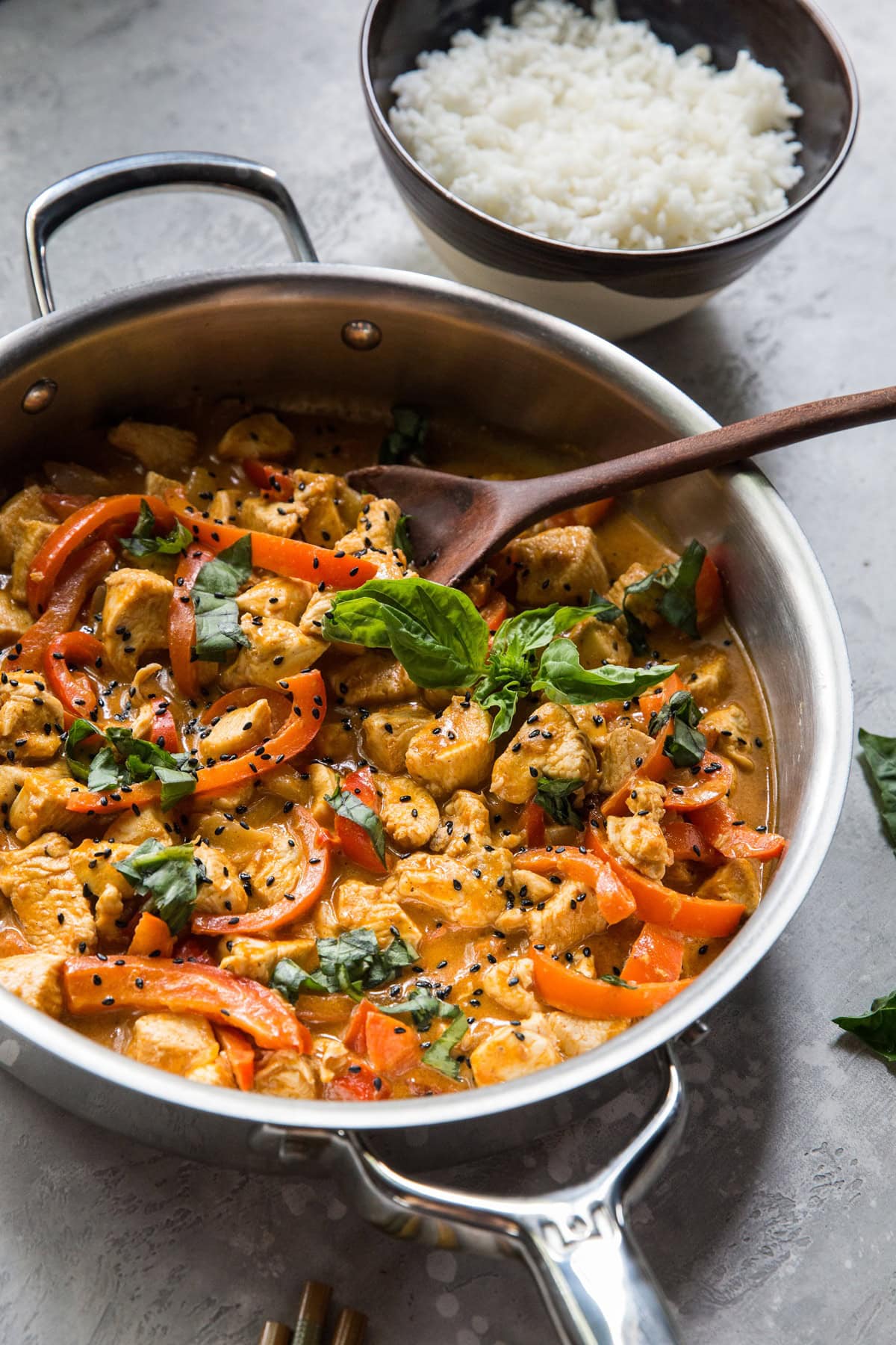 Stainless steel skillet full of creamy Panang curry with chicken, bell peppers, and basil leaves.