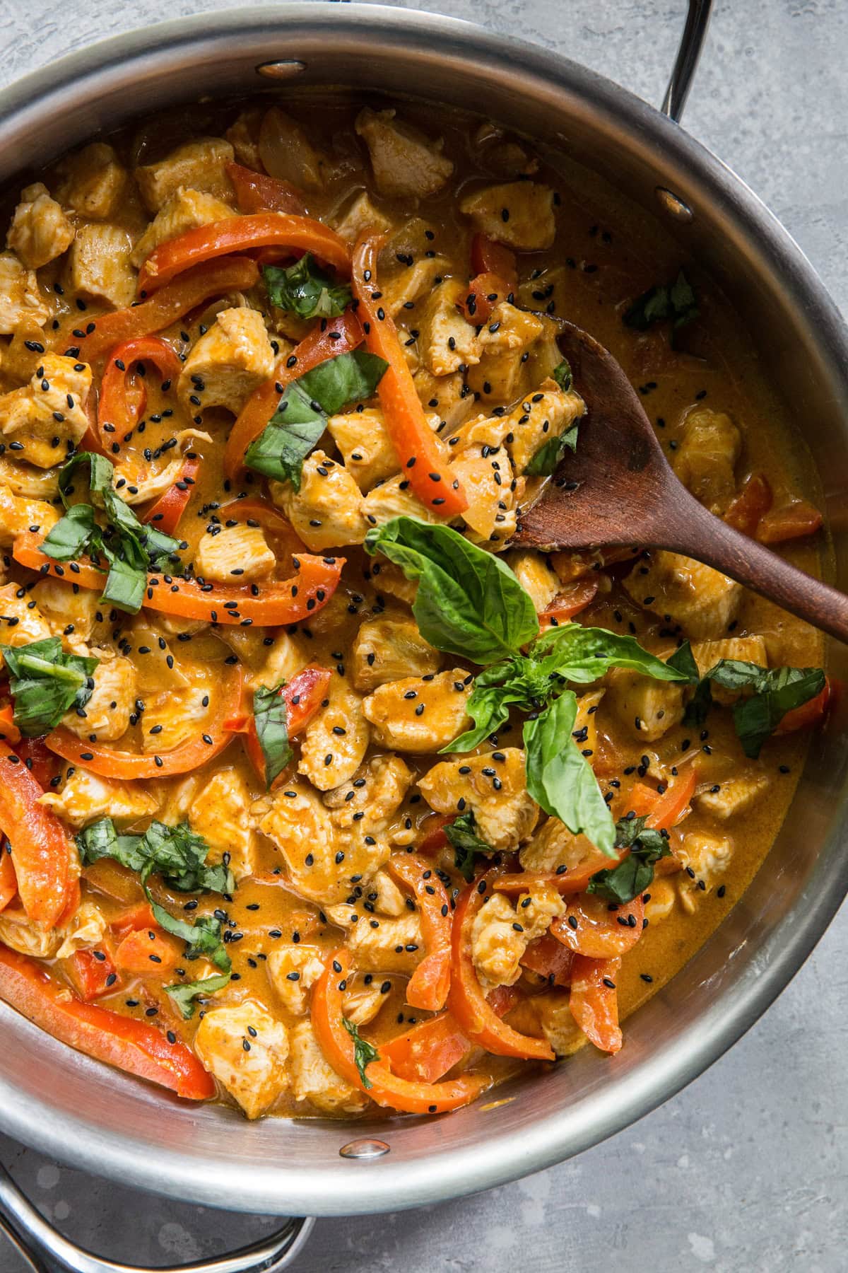 Large skillet full of chicken panang curry with a fresh basil leaf on top. A serving spoon, ready to serve.