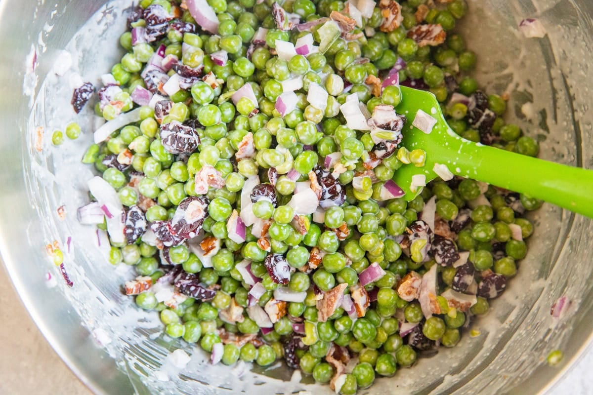 Pea Salad mixed up in a stainless steel mixing bowl with a rubber spatula, ready to use now.