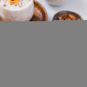 Overnight oats in three glasses with peaches and pecans on top.