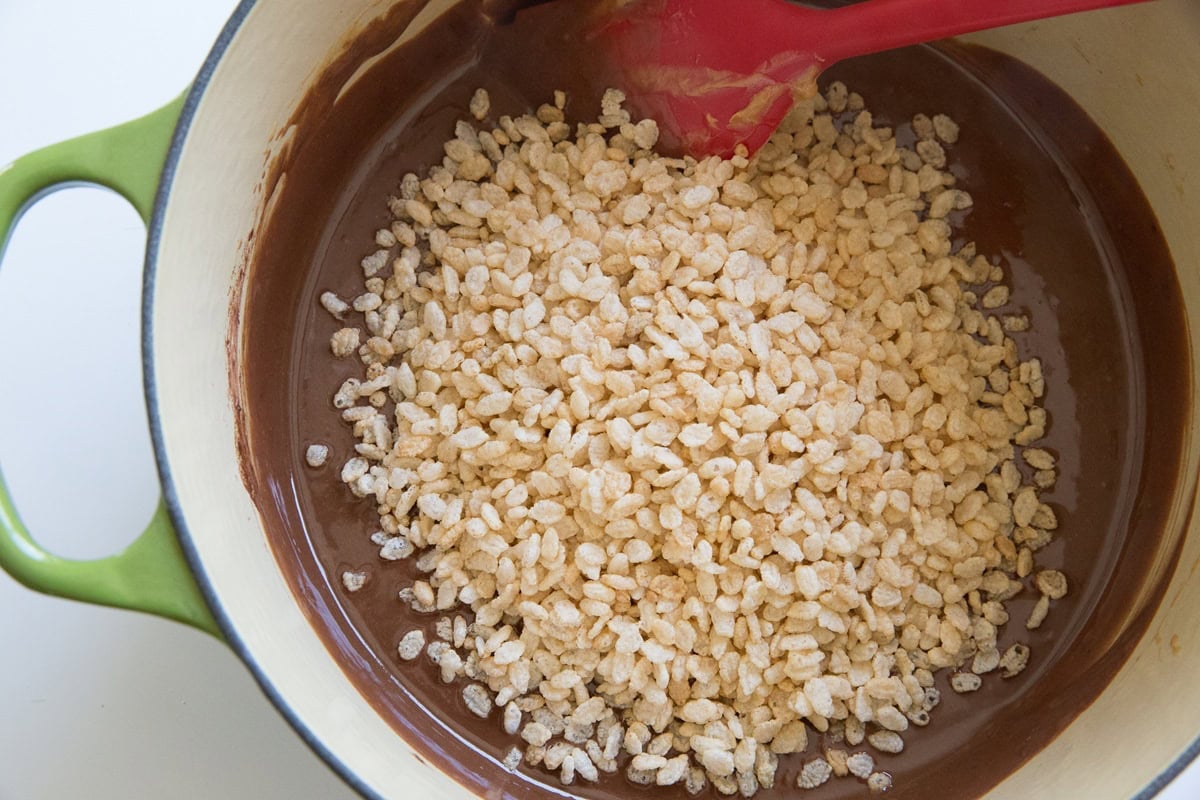 crispy rice cereal on top of a melted chocolate mixture in a large pot.