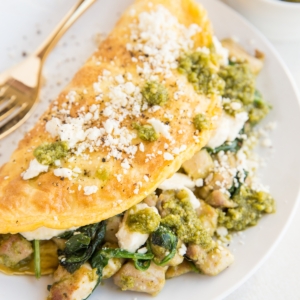 Pesto Chicken Omelette with spinach and feta on a white plate with a napkin to the side.