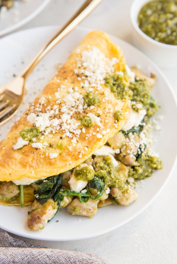 Pesto Chicken Omelette with spinach and feta on a white plate with a napkin to the side.