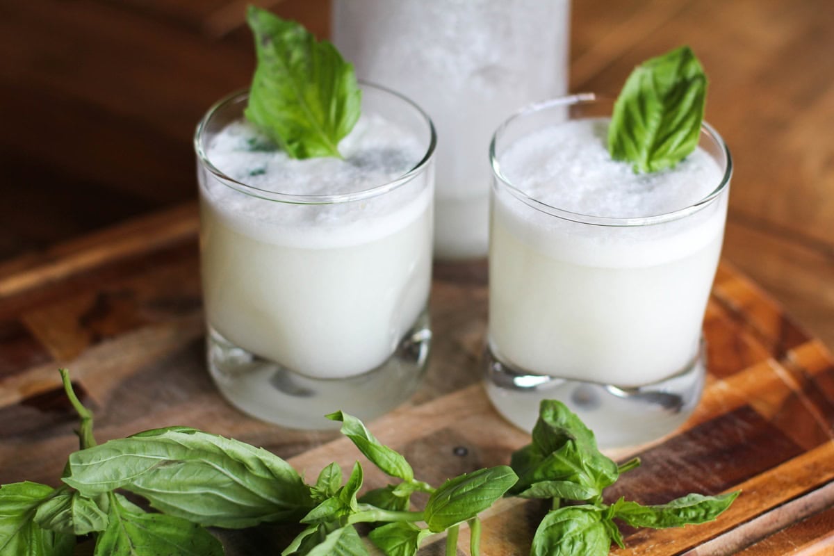 closeup glass of coconut basil ginger beer with a glass and bottle in the background