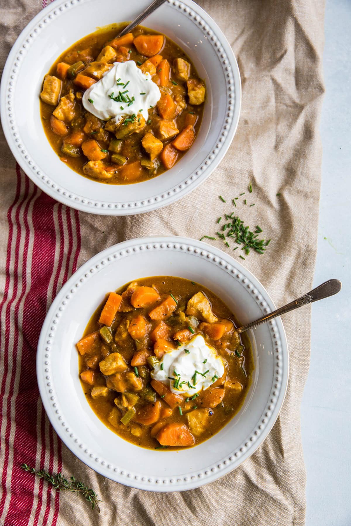 Two white bowls of pumpkin chicken chili with a burlap looking napkin underneath the bowls and fresh thyme to the side. Ready to serve.